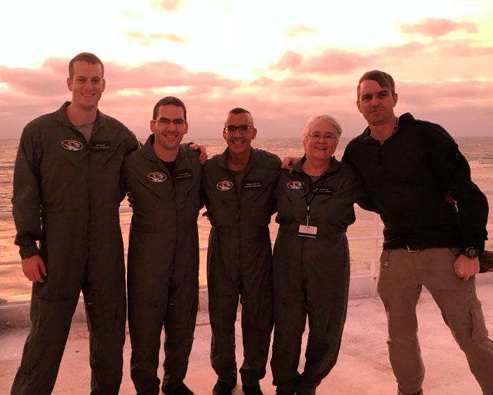 5 people in flight suits standing by the ocean